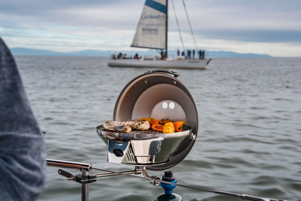 Person squeezing lemon on shrimp and vegetables on a grill by the water.